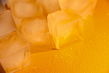 Pieces of ice on a bright background with water drops. Orange fresh background with ice flakes