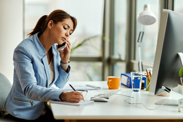 Businesswoman taking notes while making a phone call in the office.