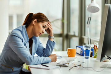 Young distraught businesswoman thinking while sitting at her office desk.