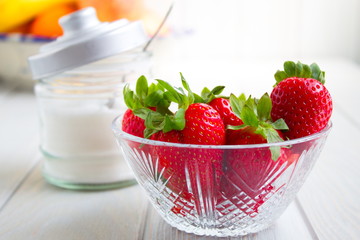 delicious red strawberries next to bowl with sugar and a spoon