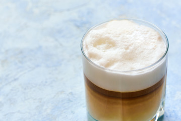 cappuccino in a glass cup prepared in a home coffee machine on a blue background.