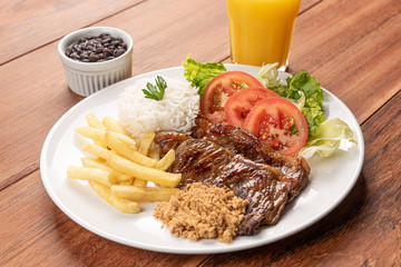 Beef steak with french fries, Beans and rice and a glass of orange juice on wooden table background, soft light