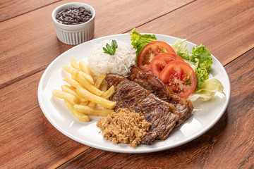 Beef steak with french fries, Beans and rice and a glass of orange juice on wooden table background, soft light