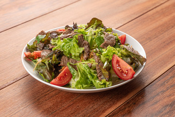 Fresh green salad with arugula,romaine, tomato, steak mignon and lettuce in a bowl on a wooden  background