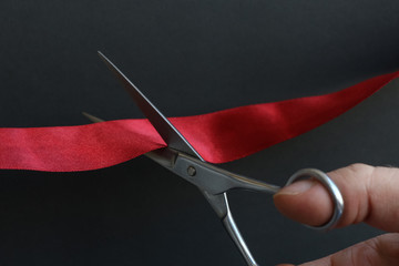 Businessman cuts a red silk ribbon with metal scissors on a black background. Theme of opening a new enterprise.