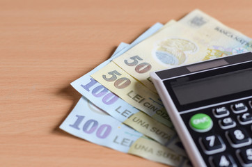 Close-up  of Romanian lei     and  handheld mini calculator  oh wooden background .