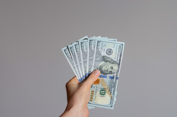 Close up view of a woman's hand holding a pile of 100 dollar banknotes   money on a gray background . The economic impact of coronavirus  in  United state of  America .