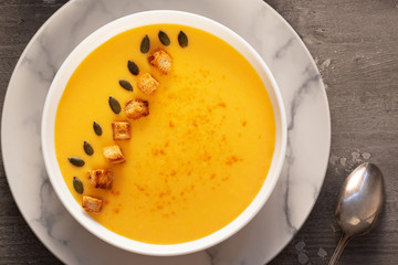 cream pumpkin soup with seeds, pepper and bread on a wooden table.
