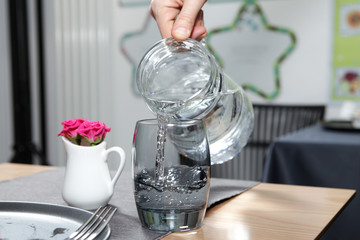 Female hand pours clear transparent water from a jug into a dark glass. Closeup