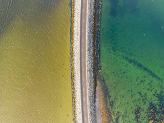 Drone shot taken in Scotland. View on a road separating the sea from the lake. Two different water colors. 