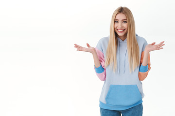 Silly giggling cute blonde girl in hoodie, shrugging and spread hands sideways, smiling as saying sorry, apologizing for cant help, being clueless and unaware, standing white background