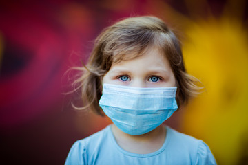 a small, beautiful girl, in a medical mask, stands on the street