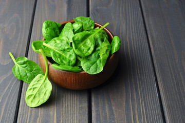 Wooden bowl with fresh spinach leaves on dark rustic background. Vegan food lifestyle concept. Copy space.