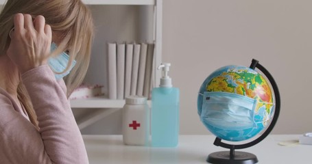 Upset Caucasian woman putting on face mask and leaving. Side view of blond lady sitting at the table with globe in protective mask on it. Covid-19 pandemic, isolation, lockdown. Cinema 4k ProRes HQ. - Powered by Adobe