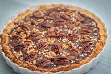 Side view of pecan pie and nuts in ceramic bowl, handmade, on striped patterned fabric