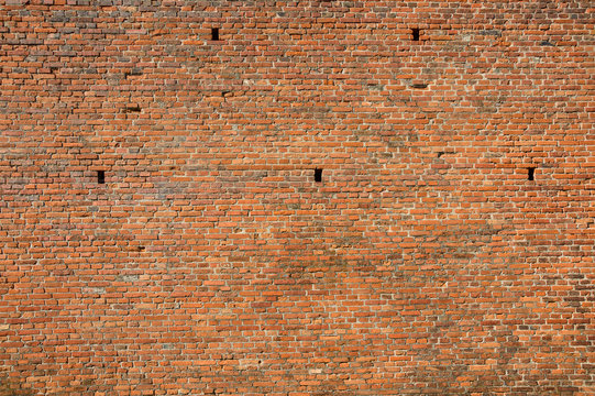 A large orange brick wall with holes in the wall.
