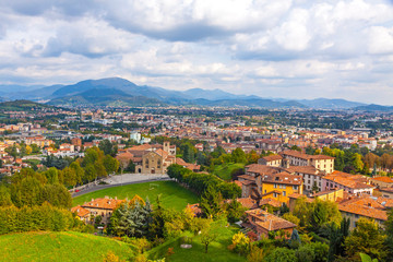Fototapeta na wymiar Aerial view of Bergamo city, Lombardy, Italy. Bergamo Alps (Alpi Orobie) begin immediately north of the city, on the background. Picturesque autumn view