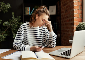 Young tired female employee resting in workplace after hard work on project in loft office.