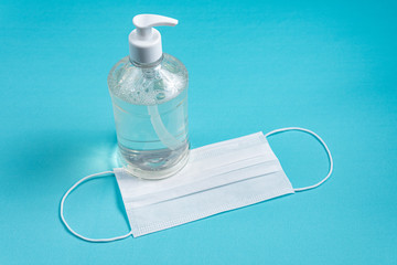 Container with alcohol gel and surgical mask on the light blue background