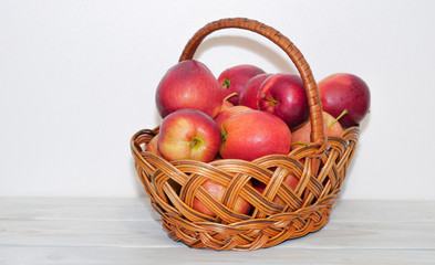 A wicker basket with red apples on a white wooden table