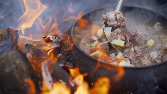 A pot of soup cooked over a fire. Stir soup with soup ladle, which is cooked in a cast iron over a fire. food in a big kettle cooked on fire