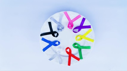 Cancer awareness concept. Stop motion of colorful ribbons on a plate rotating above table, isolated on white background. Shot in 4k resolution