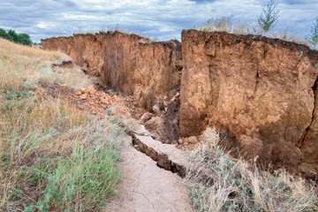 layers of earth with cracks on trail path due to landslides of the soil ecological disaster in outdoor clay wall under cloudy sky.