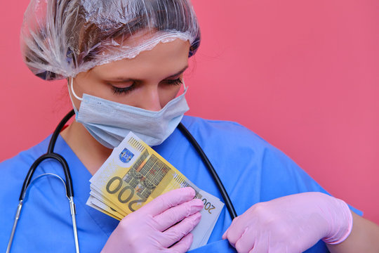 A Doctor Hides Money In A Pocket Of A Blue Uniform. A Nurse In A Medical Mask Holds A Salary In Euro Cash Notes