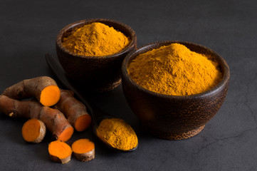 Turmeric powder in a black wooden bowl and fresh turmeric  (curcumin) rhizome on a black background,Used for cooking.