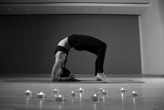 Flexible woman in yoga pose candles in fore ground, black and white image 