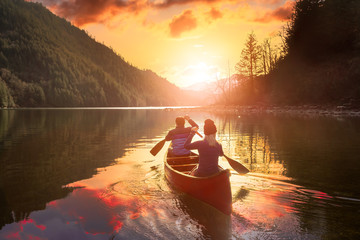 Couple friends canoeing on a wooden canoe during a colorful sunny sunset. Cloudy Sky Composite....