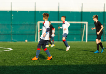 Boys in white black sportswear running on soccer field. Young footballers dribble and kick football ball in game. Training, active lifestyle, sport, children activity concept