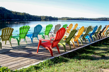 Colourful plastic lawn chairs lined up on a dock to enjoy the view of a lake and trees in Ontario, Canada.