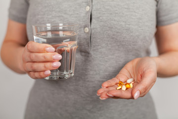 Female hands hold pills and a stock of water. Health care, medical supplement concept.