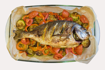 Top view on a glass dish with baked dorado fish with lemon and vegetables.