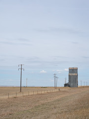 Fototapeta na wymiar Old Metal Grain Elevator on the Prairie with power poles and field with dried grass in the foreground.