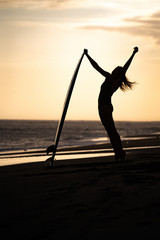 silhouette of a woman dancing with surfboard on the beach at sunset