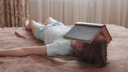 Face sleeping girl covered opened book in home bedroom. Young girl lying on bed with opened book on face - Powered by Adobe