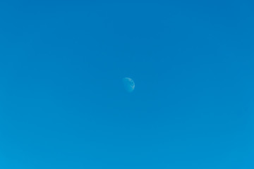 A wide angle minimalist shot of the full moon against the background of the bright blue sky in the early evening