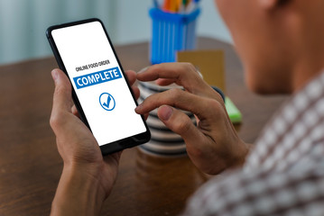 Young man asian using mobile phone using app makes order from food delivery service working from home after coronavirus or covid-19 pandemic.