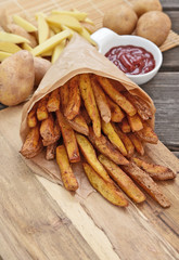 Homemade Crispy Seasoned French Fries..French fries  with spicy seasoning in brown paper bag on wooden broad.