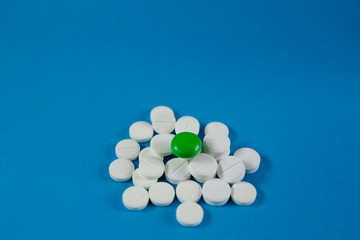 heap of white pills and one green, on a blue background