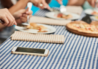 Smartphone lying on table while women eating pizza, closeup photo