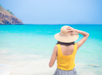 Woman with hat standing on blur image of on blue sea background. Summer and holiday concept.