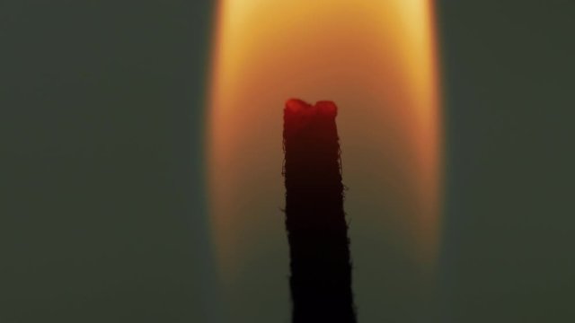 Extreme close up of flame burning the tip of an isolated vertical wick and blowing in breeze