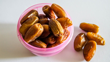 Dates or kurma in purple plastic container on isolated white background.