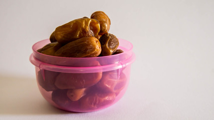 Dates or kurma in purple plastic container on isolated white background.