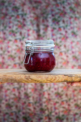 Female hands holding a home made vegan raw raspberry jam in a glass jar. Healthy raw jam in a cup with spring colors.
