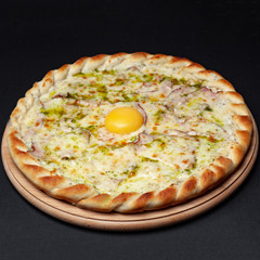 Delicious pizza carbonara served on a wooden plate isolated on black