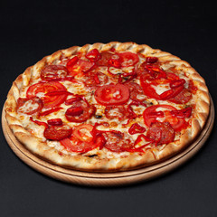 Delicious pepperoni pizza served on a wooden plate isolated on black